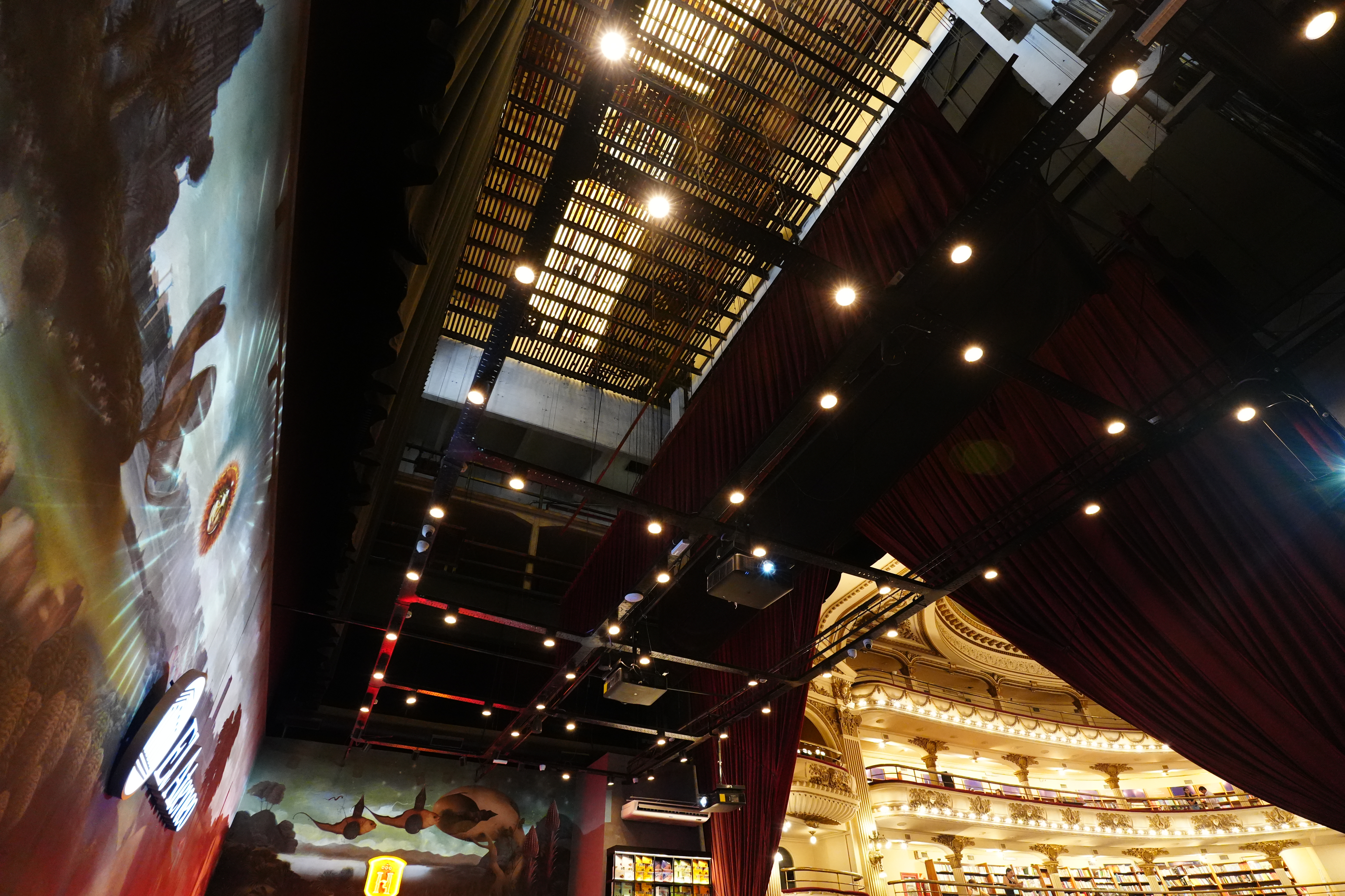 Interior view looking up at ceiling rigging and suspended bookshelf installation above the Havanna café stage.
