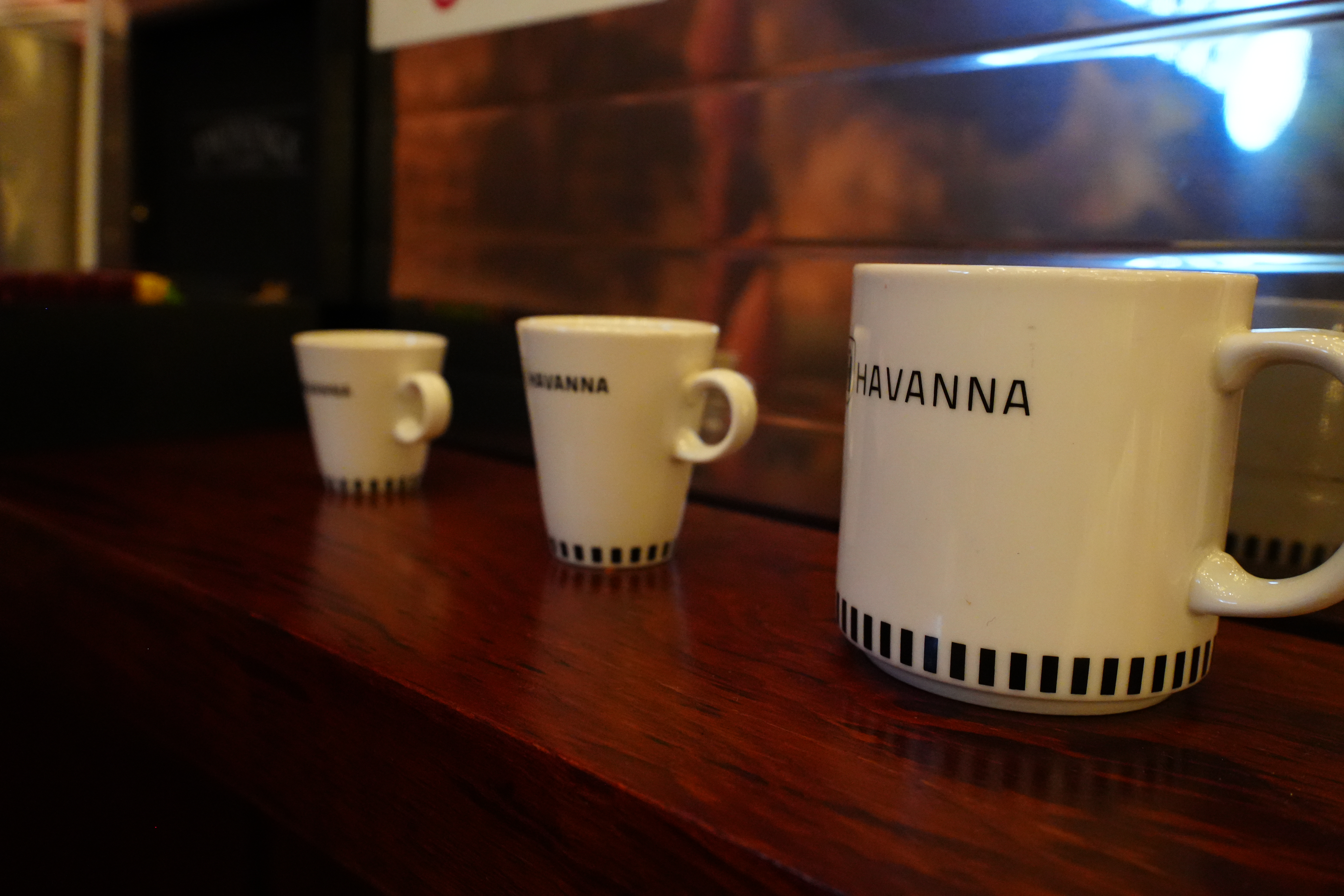 Stacked white Havanna coffee mugs on a wooden bar.