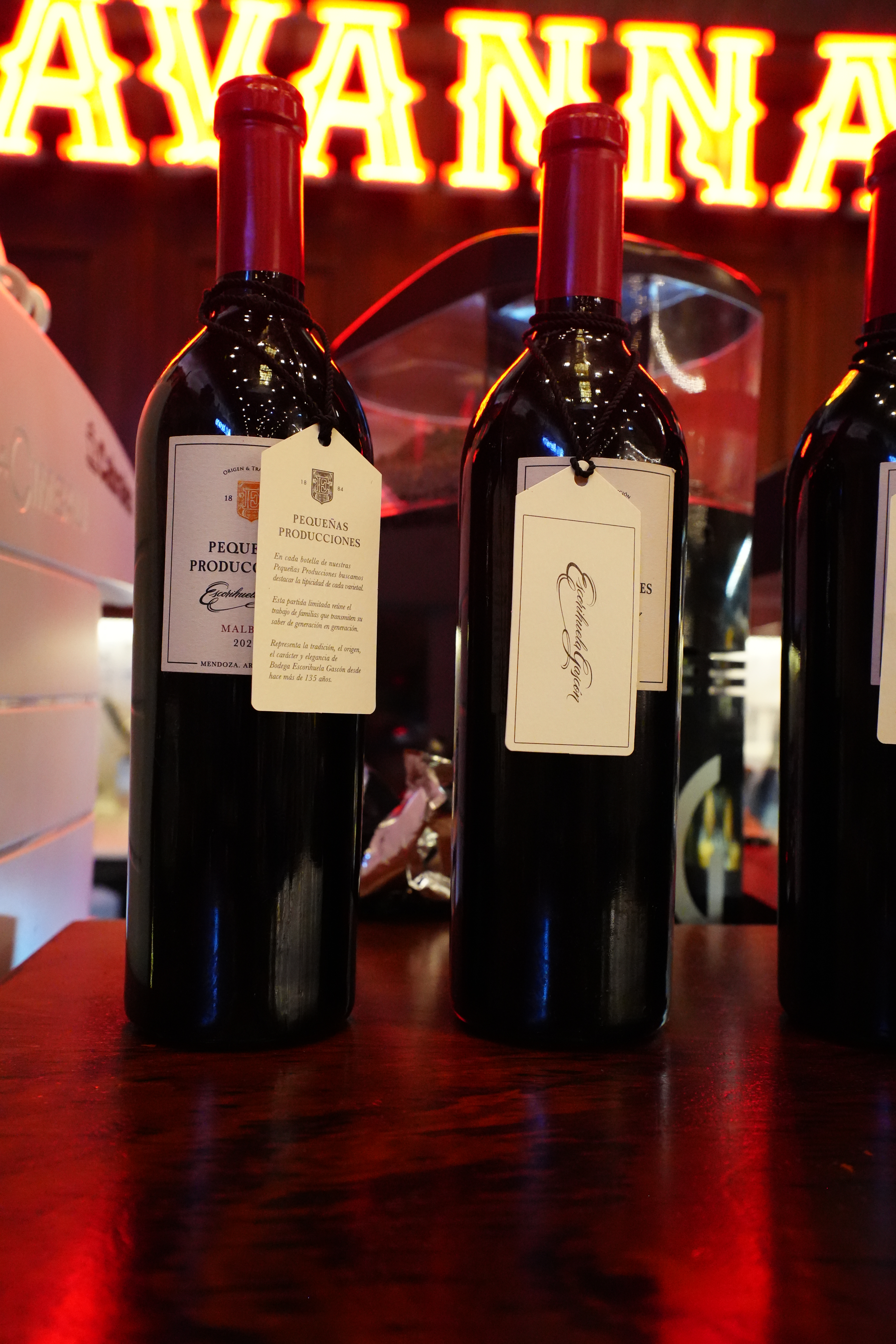 Red wine bottles standing on a dark wood counter.