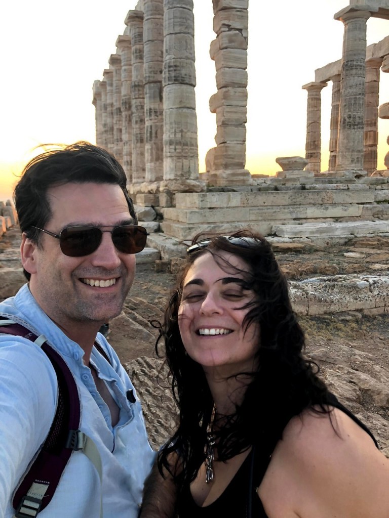Couple laughing in the wind with the Temple of Poseidon behind them